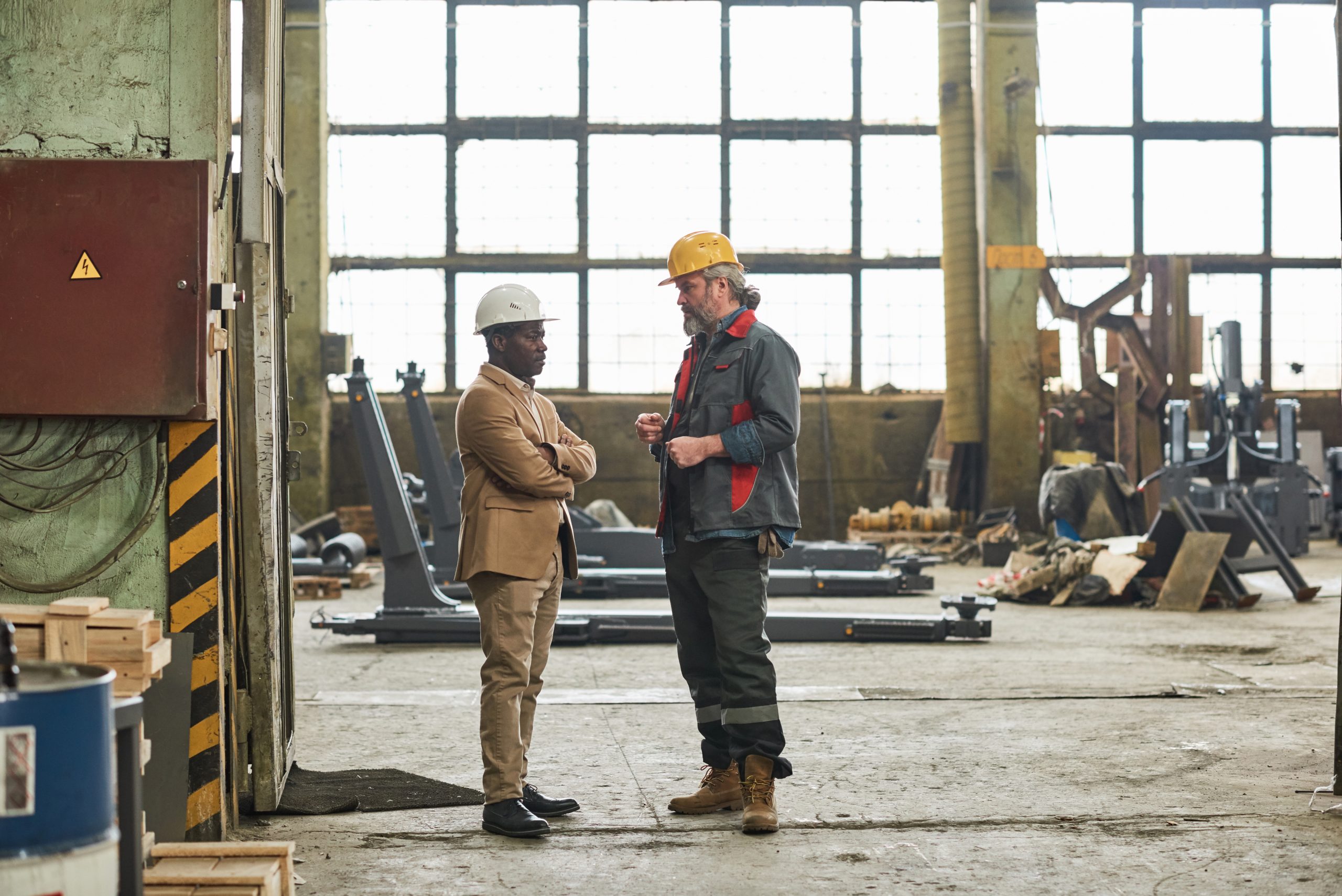 African foreman discussing the work with worker in uniform while they standing in empty workshop